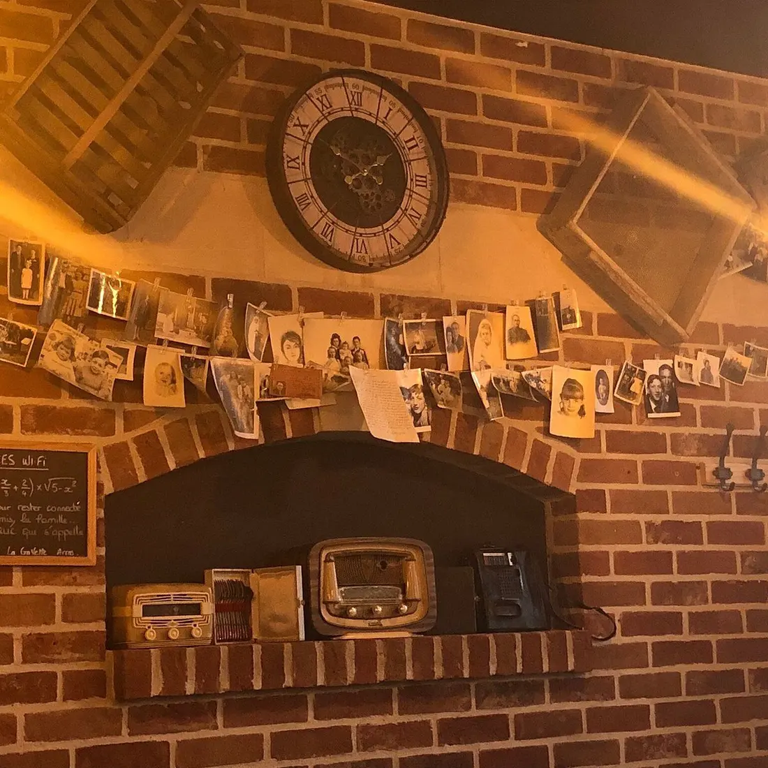 Le mur de briques de la salle, garni de photographies de famille anciennes, d'une horloge et de postes de radio d'époque.